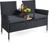 A black rattan loveseat with gray cushions and a built-in side table holding drinks and fruit. Produktbild-Vorschau