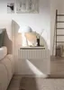 A bedside table with a lamp, vase, and glass next to a bed. Produktbild-Vorschau