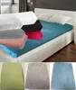 A bed with a teal fitted sheet and several folded fitted sheets in different colors stacked on top. Below are three folded fitted sheets in green, gray, and blue.