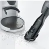 A close-up shot of a black handheld vacuum cleaner with a brush attachment cleaning coffee grounds from a silver and black coffee machine drip tray and the surrounding white surface. Podgląd zdjęcia produktu
