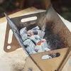 Tragbarer Metall-Holzkohlegrill mit glühender Glut und weißer Asche, auf einer hellen Fläche Anteprima dell’immagine prodotto