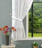A curtain with a star and moon pattern is tied back with a decorative tie, next to a window with a view of trees and water. A vase of flowers and a decorative lantern are on a table in the foreground. Produktbild-Vorschau