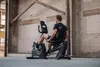 A man is exercising on a recumbent exercise bike in a large, industrial-style room with brick walls and wooden beams. Produktbild-Vorschau