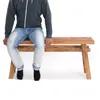 A person is sitting on a wooden bench against a white background. Produktbild-Vorschau