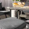 A close-up view of a grey cushion on a rattan furniture set, with a table and basket of bread in the background. Náhled obrázku produktu