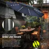 An outdoor patio scene with a table and chairs under a large navy blue cantilever umbrella with LED lights. Voir les images du produit