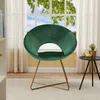 A green velvet accent chair with gold metal legs is placed in a well-lit room with sheer curtains and a window in the background. Produktbild-Vorschau