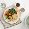 A plate of food with couscous, broccoli, and pumpkin, served with a small bowl of dressing and sesame seeds. Anteprima dell’immagine prodotto