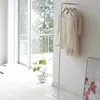 A minimalist interior scene with a white floor, a large window with a view of trees, and a white garment rack with clothes hanging on it. Anteprima dell’immagine prodotto