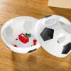 A soccer ball shaped container with a pencil sharpener and push pins inside, resting on a wooden surface. Produktbild-Vorschau