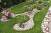 A landscaped garden with a curved lawn border made of small stones and plants. Podgląd zdjęcia produktu