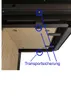 A close-up view of the underside of a fireplace, highlighting a transport securing mechanism with blue arrows and text. Produktbild-Vorschau