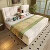 A bedroom scene with a bed as the main focus, featuring a headboard with integrated charging ports and a bedside shelf. The bed is made with a beige upholstered frame and a comforter with green and yellow accents. There are decorative pillows and charging  Anteprima dell’immagine prodotto