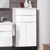 A white bathroom cabinet with drawers and doors, placed next to a white vanity. The wall behind is tiled with dark gray rectangular tiles. Two decorative vases and a red glass are on top of the cabinet. Produktbild-Vorschau