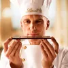 A chef in a white uniform and hat is holding a bar of dark chocolate and smelling it. Produktbild-Vorschau