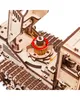 A close-up view of a wooden model of a self-propelled mower, focusing on the tracked wheels and a central rotating mechanism. Podgląd zdjęcia produktu