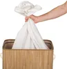 A hand is holding a white laundry bag over a bamboo laundry basket. Náhled obrázku produktu