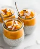 Three jars of chia pudding topped with mango puree and coconut flakes, with spoons in two of the jars. Podgląd zdjęcia produktu