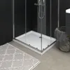 A modern bathroom scene featuring a white shower tray with an anti-slip surface, a shower fixture, a grey rug, and a woven basket with a towel. Produktbild-Vorschau