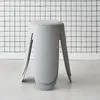 A light gray stool with a textured bouclé seat sits in front of a white wall with a black grid pattern. The stool has four legs that splay outwards. Produktbild-Vorschau