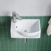 A white ceramic sink with a chrome faucet is mounted on a wall with green tiles. Produktbild-Vorschau