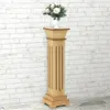 A wooden plant stand with a vase of white flowers on top, set against a white brick wall. Náhľad obrázku produktu