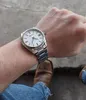 A person's wrist wearing a silver watch with a white face, with jeans and brown boots visible. Náhľad obrázku produktu