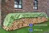 A stack of firewood covered by a tarp with a green grass pattern, placed against a brick wall. Produktbild-Vorschau