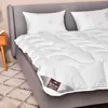 A neatly made bed with white bedding and pillows, featuring a close-up of a duvet with a brand tag. Produktbild-Vorschau