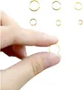 A hand is holding a small gold ring, with several other gold rings of varying sizes scattered in the background. Produktbild-Vorschau