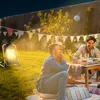 People enjoying a backyard gathering at night, illuminated by a work light. Produktbild-Vorschau