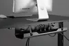 A close-up view of a cable management tray mounted under a desk, holding various cables and power strips. A computer monitor and mouse are visible on the desk surface above. Produktbild-Vorschau