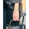 A person wearing a watch and holding a handbag. Produktbild-Vorschau