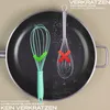 A split image showing a comparison of two whisks on a frying pan. One whisk is turquoise and has a green checkmark, indicating it is safe for the pan. The other whisk is silver and has a red cross, indicating it is not safe. Text overlays explain the benef Anteprima dell’immagine prodotto