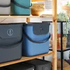 Several storage boxes are neatly arranged on wooden shelves, with some wooden bowls and plants visible in the background. Produktbild-Vorschau