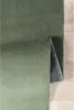 A green rug is shown with a corner lifted, revealing its anti-slip backing. The rug is placed on a wooden floor. Produktbild-Vorschau