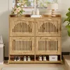 A wooden shoe cabinet with metal legs and gold handles, placed in a room with a window and plants. Voir les images du produit