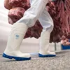 A person wearing white protective clothing and white boots with blue soles walks through a facility, carrying large cuts of meat. Produktbild-Vorschau