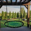 A round net swing hanging from a wooden pergola in a backyard setting with trees and grass. Voir les images du produit