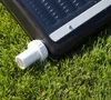 A close-up of a solar collector with a white pipe fitting attached, resting on green grass. Podgląd zdjęcia produktu