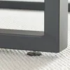 A close-up view of the base of a black metal table leg with an adjustable foot on a textured white carpet. Voir les images du produit