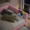 A pink daybed with pillows and a tablet charging on the headboard, next to a window with a city view at night. Podgląd zdjęcia produktu