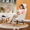 A woman is reading a book while sitting in a rocking chair with a footstool next to her. Náhľad obrázku produktu