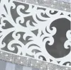 A close-up view of a white table runner with a decorative cut-out pattern and a silver band with rhinestones along the top edge. Náhľad obrázku produktu