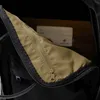 Close-up view of the interior of a black backpack, showing a zippered pocket with a tan lining and a white card inside. Anteprima dell’immagine prodotto