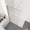 A modern bathroom shower enclosure with a glass screen and a white shower tray, set against white subway tiles and a black and white geometric floor. Produktbild-Vorschau