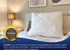 A white pillow on a bed with a bedside lamp and framed artwork in the background. Produktbild-Vorschau
