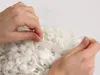 Hands opening a clear plastic bag filled with white foam flakes. Produktbild-Vorschau