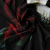 A close-up, draped view of a black fabric with a printed pattern of red roses and a skull. The fabric is folded and creased, creating shadows and highlights. Produktbild-Vorschau