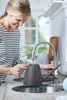 A woman is filling a watering can at a kitchen sink. Náhled obrázku produktu